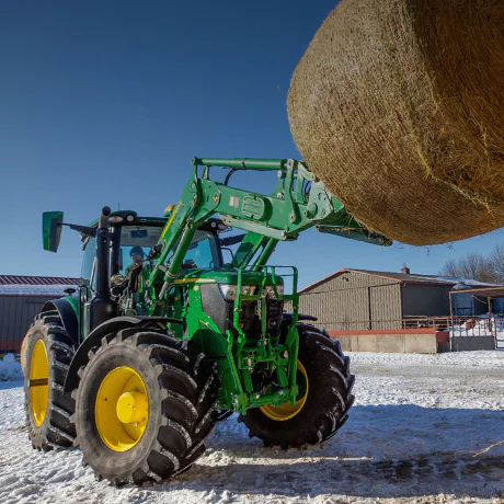 tractor lifting round hay bale with front loader